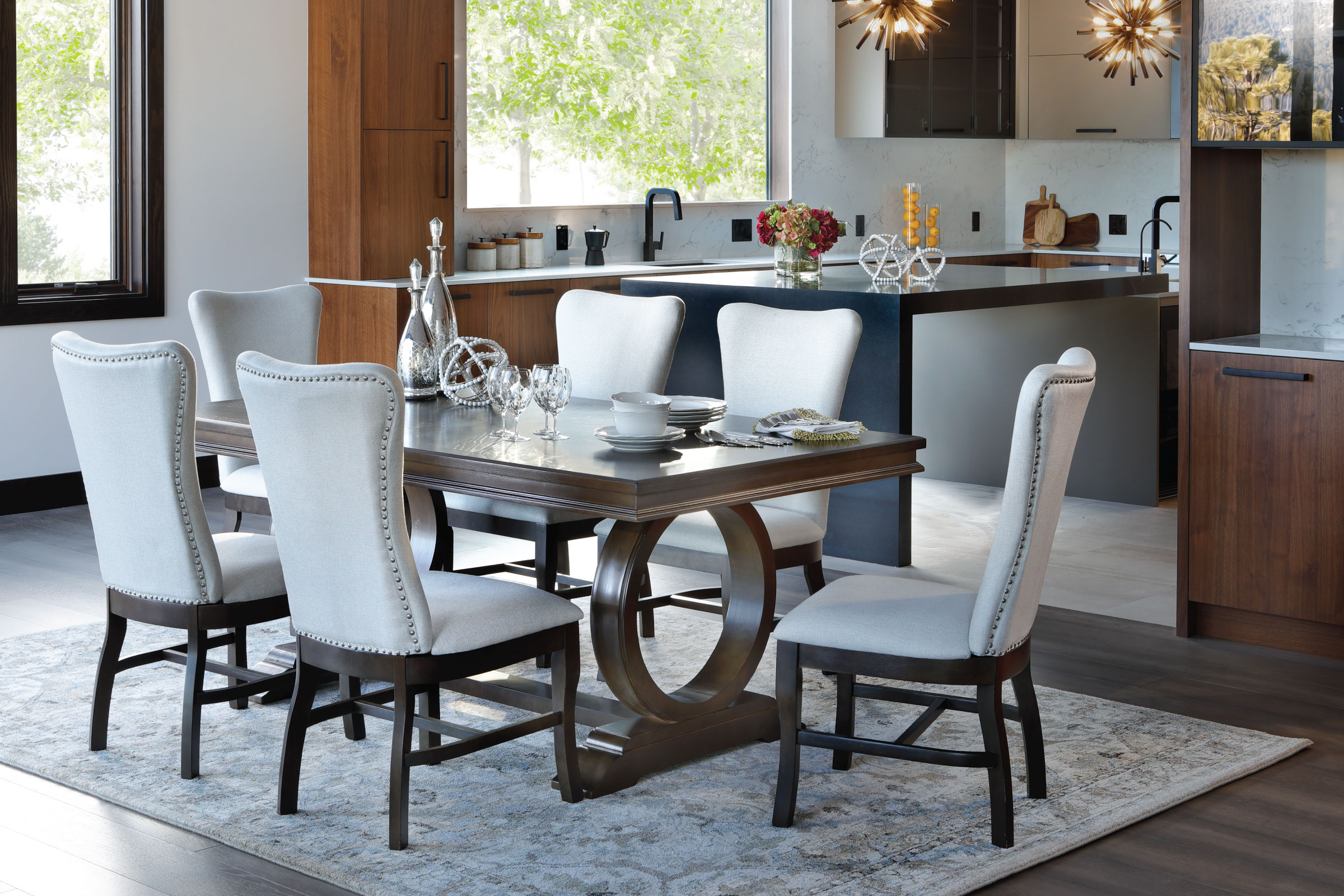 Brown wood Dining Table with hollow circular base and white fabric parsons chairs.